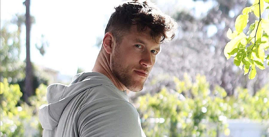 A photo of Clayton Echard. A man with curly brown hair wearing a grey t shirt