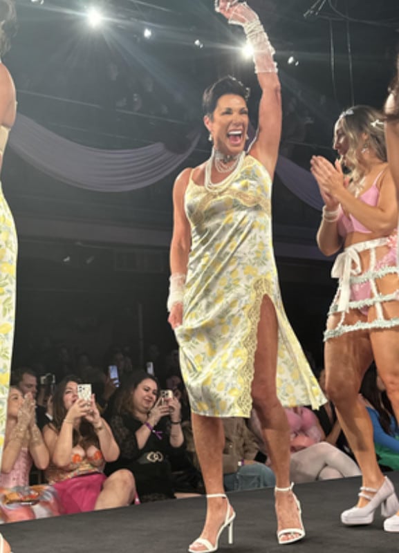 An older woman with black hair in a short yellow dress.